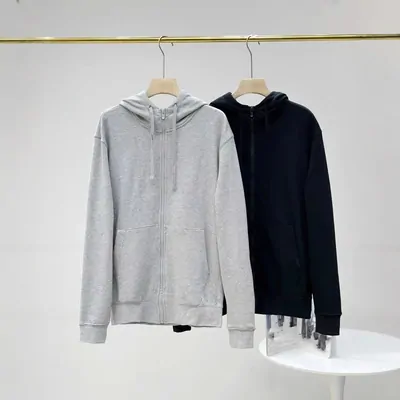 Two zip-up hoodies on wooden hangers hung from a gold rail, one light gray and one dark navy, above a small round white table.