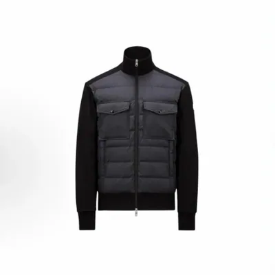 A jacket built from a quilted charcoal front panel with two chest pockets, black sleeves and a black stand collar, zipped shut on white.