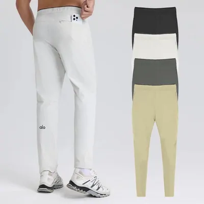 A model photographed from the chest down in white straight-leg sweatpants and white sneakers, with the same pants folded beside him in gray, cream and pale yellow.