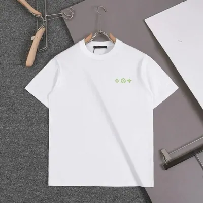 A white T-shirt on a wooden hanger laid out on gray felt, a small green mark printed high on the chest, a second hanger beside it.